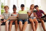 Group Of Children Sit On Window Seat And Use Technology