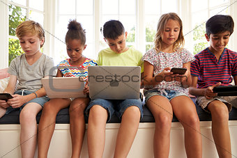Group Of Children Sit On Window Seat And Use Technology