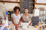 Two women ready to serve behind the counter at a coffee shop