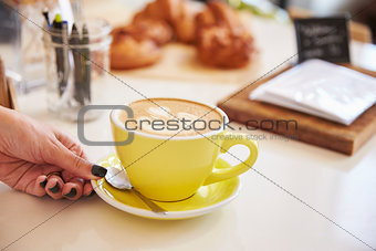 WomanÕs hand and cappuccino coffee in yellow cup and saucer