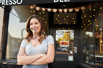 Female business owner stands outside cafe with arms crossed