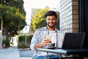 Bearded young man looking at his smartphone outside a cafe