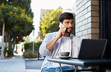 Bearded young man with laptop on the phone outside a cafe