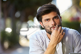 Pensive looking bearded young man sitting outside, portrait