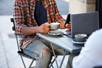 Low section crop of two adult men sitting outside a cafe