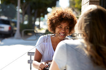 Two female friends sitting at a table outside a cafe
