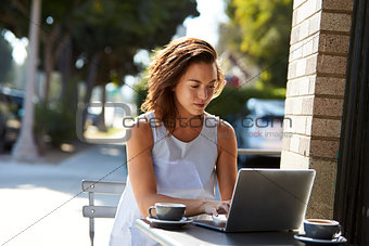 Young white woman using a laptop at a table outside a cafe
