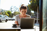 Young woman with hair in a bun using a laptop outside a cafe