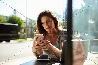 Young white woman using smartphone at a table outside a cafe