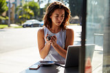 Young white woman with coffee looks at laptop outside a cafe