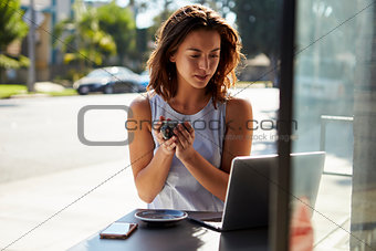 Young white woman with coffee looks at laptop outside a cafe