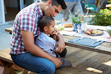 Father And Son Sitting At Table For Outdoor Meal In Garden