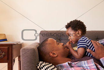 Father And Son Relaxing On Sofa At Home Together