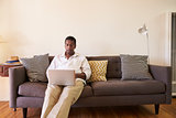 Senior Man Sitting On Sofa At Home Using Laptop