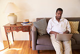 Senior Man Sitting On Sofa At Home Using Laptop