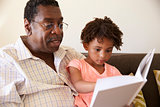 Grandfather And Granddaughter Reading Book At Home Together