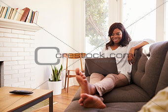 Woman Relaxing On Sofa At Home Using Laptop