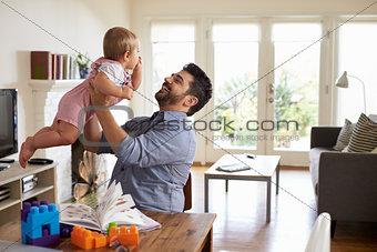 Father Sits At Table And Plays With Baby Son At Home