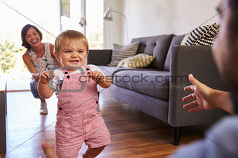 Parents Watching Baby Daughter Take First Steps At Home