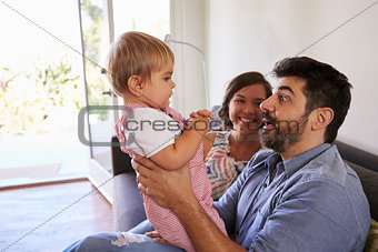 Parents Playing With Baby Daughter On Sofa At Home
