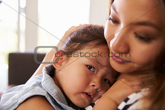 Mother Cuddling Daughter On Sofa At Home