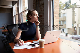 Thoughtful Businesswoman Working On Laptop By Window