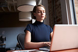 Businesswoman Sitting At Desk By Window Working On Laptop