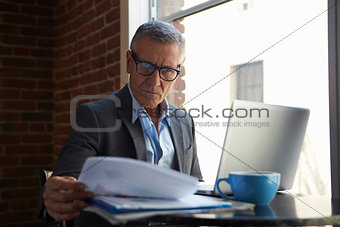 Mature Businessman Working On Laptop By Office Window