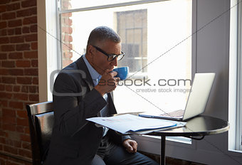 Mature Businessman Working On Laptop By Office Window