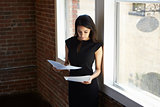 Businesswoman Reading Document Standing By Office Window