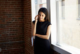 Businesswoman Making Phone Call Standing By Office Window