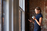 Businesswoman Checking Phone Standing By Office Window