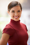Smiling young white businesswoman in maroon dress, vertical