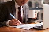 Businessman working on document holding coffee mug, close up