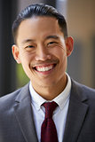 Young Asian businessman smiles to camera, close up, vertical