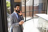 Middle aged Hispanic businessman using phone and holding cup