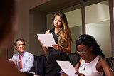 Woman stands reading document at an evening business meeting