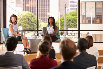 Two female speakers sit facing audience at business seminar