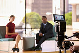 Black man and white woman on TV set, focus on foreground