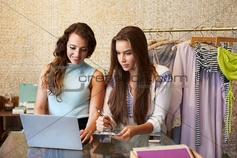 Two women working in a clothes shop using a laptop computer