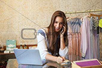 Young woman working in clothing store on phone, front view