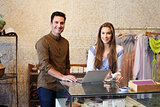 Young man and woman working in clothes shop look to camera