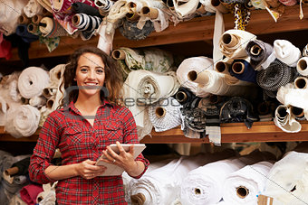 Woman using tablet in fabric storage warehouse, portrait