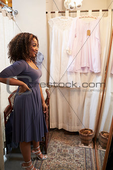 Smiling woman trying on dress in changing room, vertical