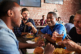 Male Friends Eating Out In Sports Bar With Screens In Behind