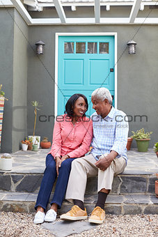 Senior couple sit on steps outside their house, vertical