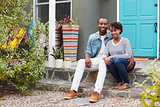 Young couple sit looking to camera outside their new house