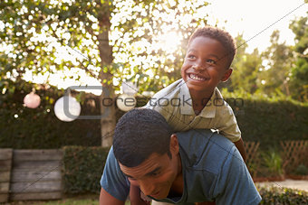 Young black boy playing on his dadÕs back in a garden