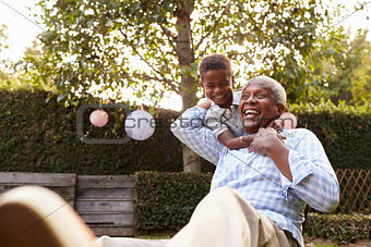 Young black boy embracing grandfather sitting in garden