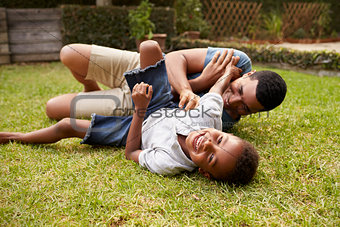 Black father and young son play lying on grass, low angle